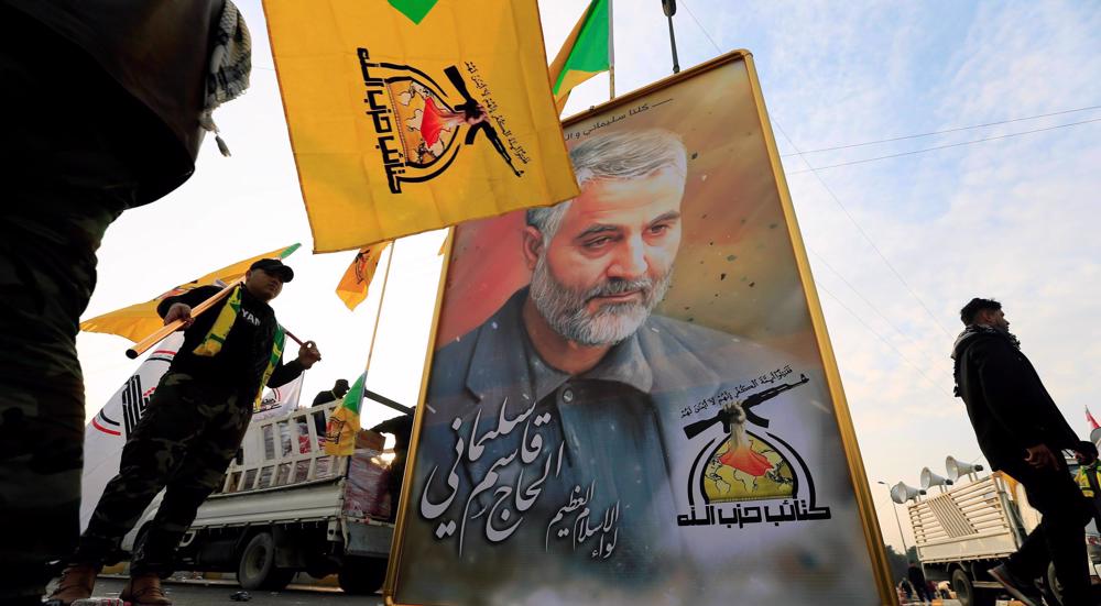 Des combattants du Kataeb Hezbollah portent des drapeau de ce groupe à côté d'un portrait du général Qassem Soleimani. (Archives)